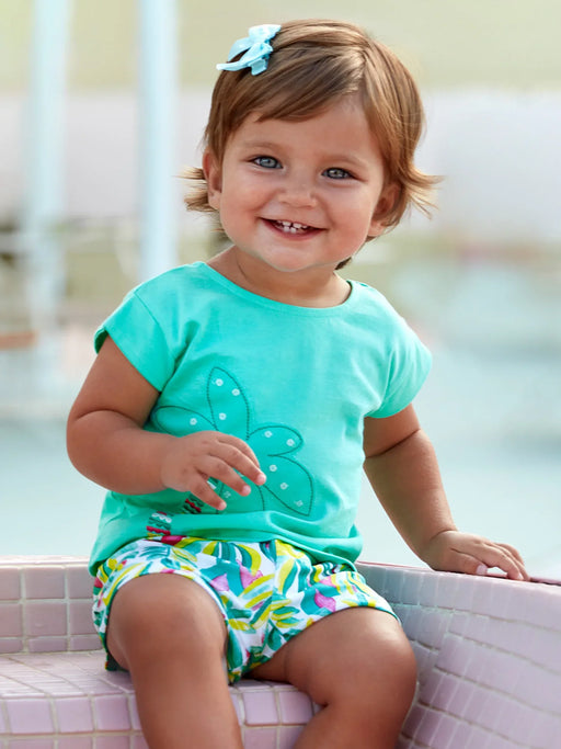 Smiling baby girl modelling the Mayoral palm tree shorts set.