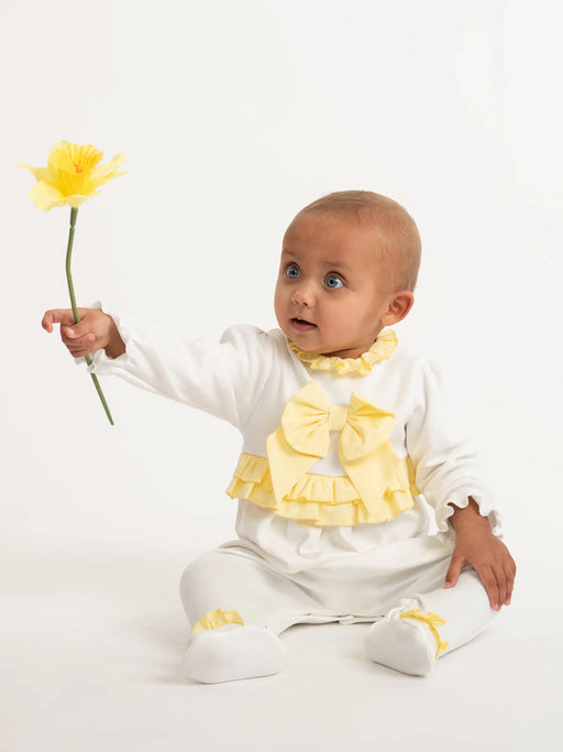 Baby girl in yellow babygrow & headband holding a yellow daffodil.