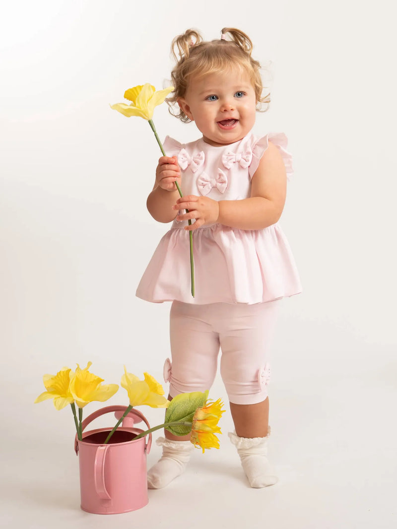 Baby girl wearing the Caramelo bow leggings set while holding a daffodil.
