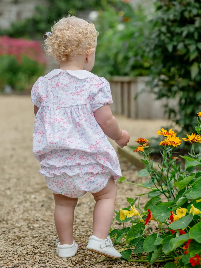 Baby girl in pink lola dress standing next to orange flowers.