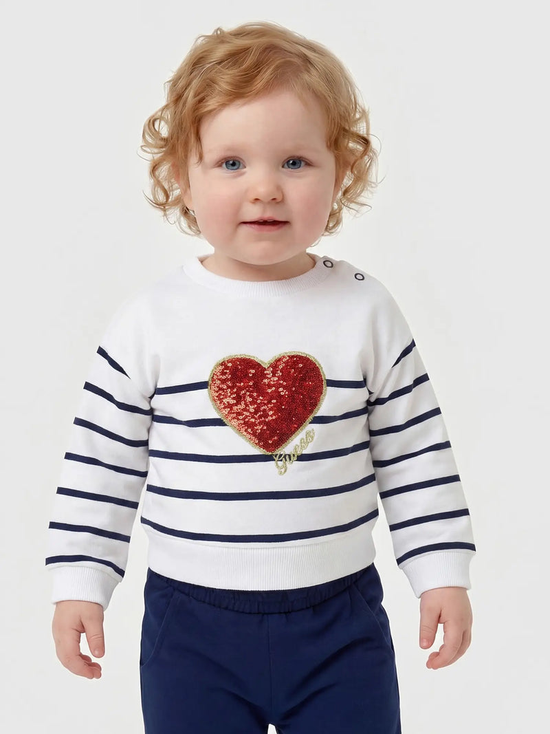 Smiling baby girl modelling the Guess glitter heart tracksuit.
