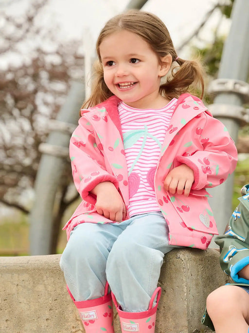 Smiling girl modelling the Hatley cherries raincoat.