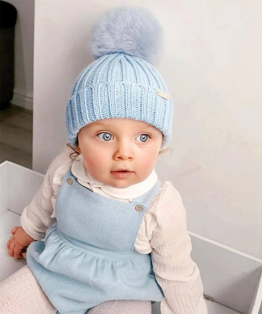 Baby girl wearing a pale blue bobble hat. 