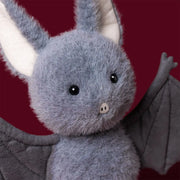 Jellycat broox bat, modelled against a dark purple background.