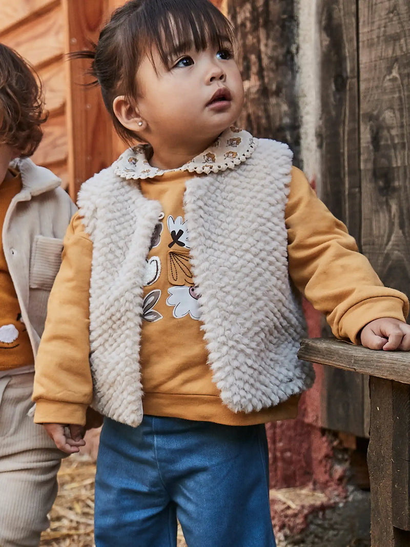 Smiling baby girl modelling the Mayoral faux fur gilet.