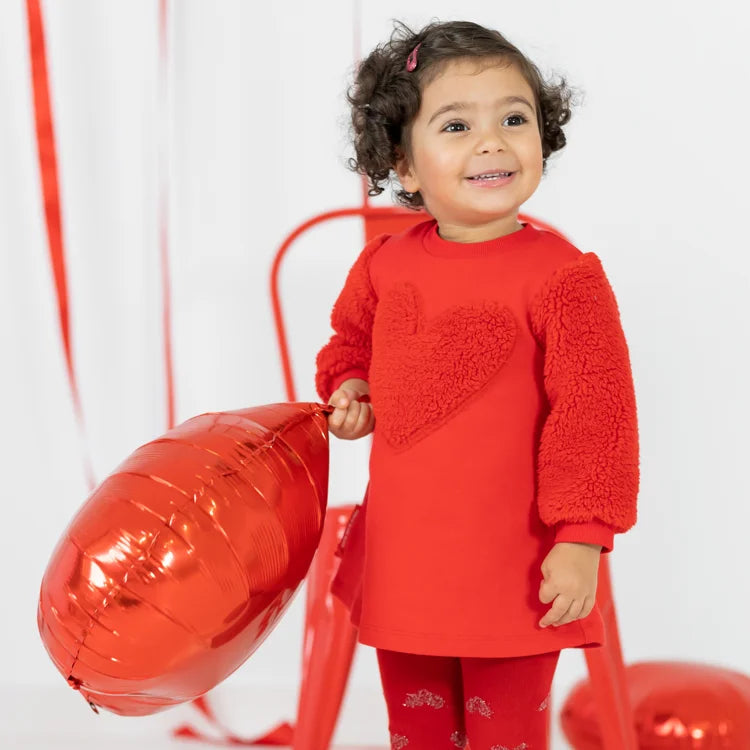 Smiling baby girl holding a red balloon while wearing a bright red dress.