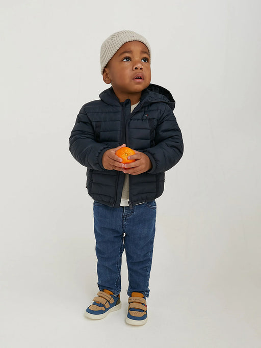 Baby boy modelling the Tommy Hilfiger puffer jacket while holding an orange.
