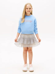 Girl in blue sequin logo sweatshirt by Tommy Hilfiger.