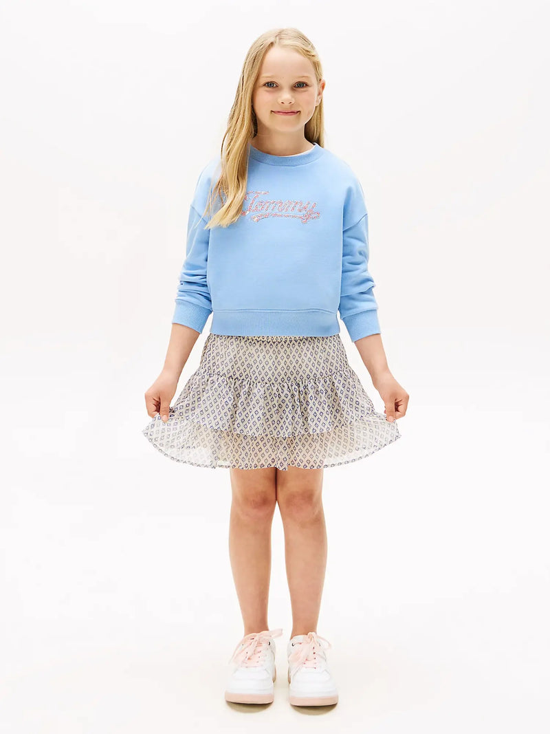 Girl in blue sequin logo sweatshirt by Tommy Hilfiger.