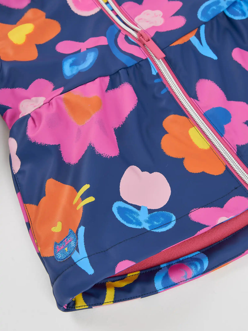 Closer look at the Tuc Tuc printed raincoat showing detail of the glitter logo patch at the hem.
