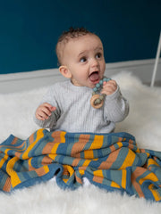 Baby boy sitting on a white faux fur rug with the Ziggle striped blanket over his knees. 