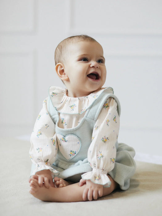 Smiling baby girl modelling the Deolinda fiona pinafore.