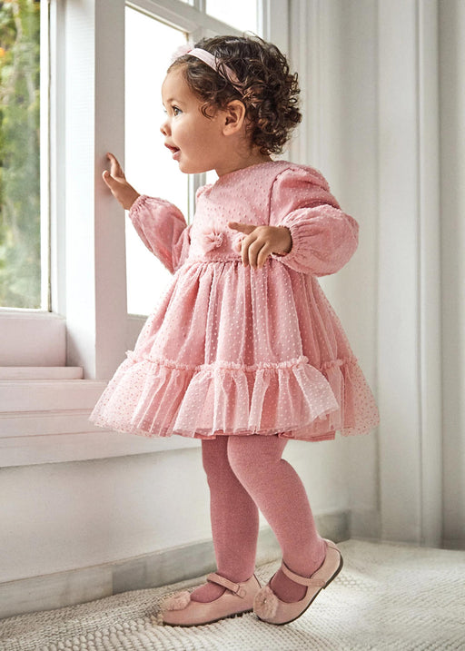Baby girl standing by a window wearing the Mayoral plumeti dress.